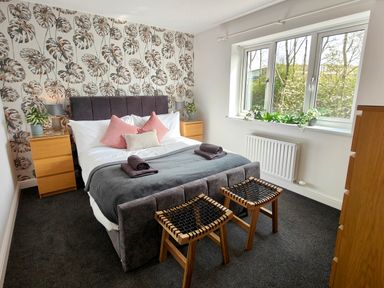 A bedroom with a bed two wooden stools bedside tables with lamps and plants and a window with plants on the sill at Sanderson House in Cleator Moor