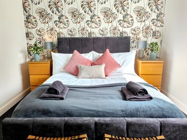 A bedroom with a double bed two bedside tables with lamps and plants and patterned wallpaper at Sanderson House in Cleator Moor