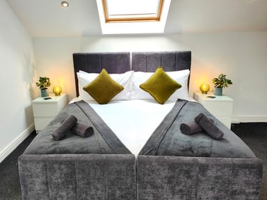 A bedroom with a double bed grey headboard grey bedding green pillows bedside tables with lamps and plants under a skylight at Sanderson House in Cleator Moor