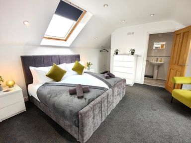 A bedroom with a bed under a skylight window a dresser plants and an open door to a bathroom at Sanderson House in Cleator Moor