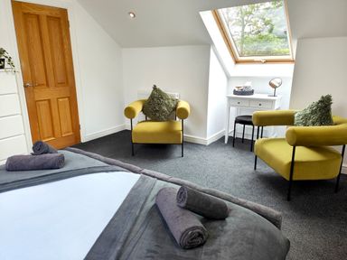 A bedroom with two yellow chairs a white dressing table with mirror and towels on a bed at Sanderson House in Cleator Moor