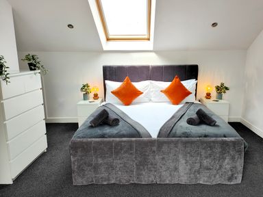A bedroom with a gray bed frame orange pillows white dresser and bedside tables with plants and lamps at Sanderson House in Cleator Moor