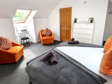 A bedroom with a bed, two orange chairs, a white dresser with plants, a small white desk under a skylight window at Sanderson House in Cleator Moor