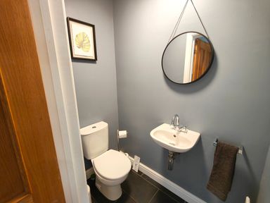 A bathroom with a toilet, sink, round mirror, towel rack with a towel, and framed artwork at Sanderson House in Cleator Moor