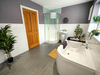 A bathroom with a bathtub a shower cubicle a sink and plants at Sanderson House in Cleator Moor