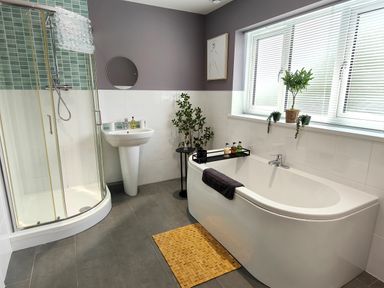 A bathroom with a bathtub a shower sink and plants on a window sill at Sanderson House in Cleator Moor