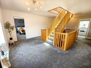 A hallway with a wooden staircase and gray carpet with doors leading to a bedroom and a bathroom at Sanderson House in Cleator Moor