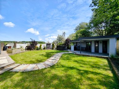 A garden with a curved stone pathway leading to a white building with a covered patio at Sanderson House in Cleator Moor
