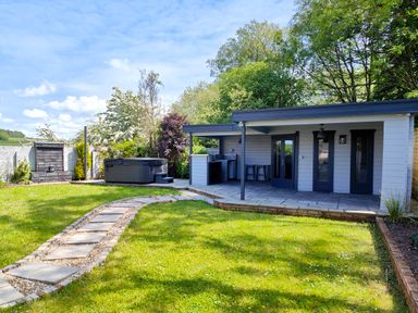 A backyard with a hot tub a stone path leading to a covered patio with bar stools and a kitchenette at Sanderson House in Cleator Moor
