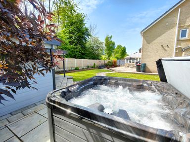 An outdoor hot tub bubbling on a patio next to a garden and a house at Sanderson House in Cleator Moor
