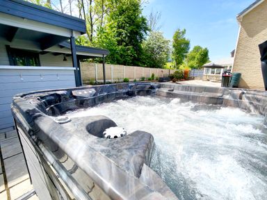 An outdoor hot tub with bubbling water near a patio and a wooden fence with trees at Sanderson House in Cleator Moor