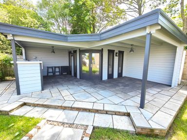 An outdoor covered patio area with a bar counter two stools and dark framed glass doors at Sanderson House in Cleator Moor