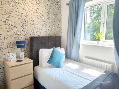 A bedroom with a single bed beside a window with blue curtains and a small wooden bedside table with a blue lamp at Sanderson House in Cleator Moor