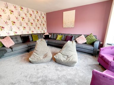 A living room with a large grey sectional sofa with various colored cushions two beige bean bags and two purple armchairs at Sanderson House in Cleator Moor