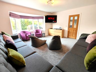 A living room with gray sofas and colorful cushions facing a wall mounted TV and two purple armchairs at Sanderson House in Cleator Moor