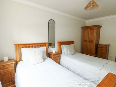 A bedroom with two beds, a wardrobe and a bedside table at Bwthyn Clai Llangefni
