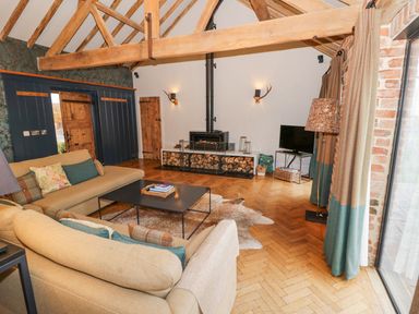A living room with exposed wooden beams a wood burning stove and beige sofas at Fairoaks Barns in Hollybush near Ledbury