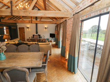 A dining and living area with wooden beams a table chairs sofas fireplace and sliding glass doors showing an outside patio at Fairoaks Barns in Hollybush near Ledbury