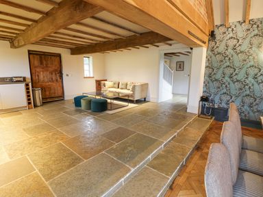 A living area with a sofa and ottomans on a tiled raised platform next to a dining area with dining chairs at Fairoaks Barns in Hollybush near Ledbury