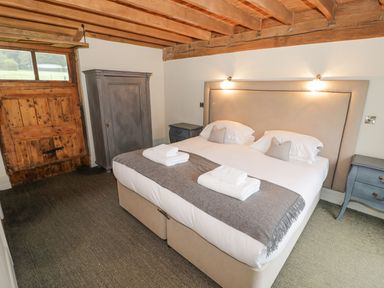 A bedroom with a double bed two bedside tables a wardrobe wooden ceiling beams and a wooden door at Fairoaks Barns in Hollybush near Ledbury