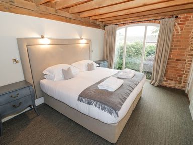 A bedroom with a double bed towels on the bed bedside tables exposed wooden beams and large window at Fairoaks Barns in Hollybush near Ledbury