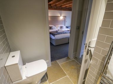 A bathroom with a toilet visible and a view into a bedroom with a bed and towels at Fairoaks Barns in Hollybush near Ledbury