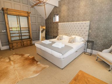 A bedroom with a large bed and headboard wooden cabinet and animal skin rug at Fairoaks Barns in Hollybush near Ledbury