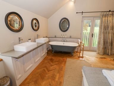 A bathroom with two sinks and mirrors a clawfoot bathtub and glass doors with curtains at Fairoaks Barns in Hollybush near Ledbury