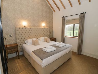 A bedroom with a large bed with pillows and towels bedside tables and a window with curtains at Fairoaks Barns in Hollybush near Ledbury