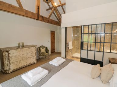 A bedroom with a bed and folded towels a chair and a dresser with exposed wooden beams and an adjoining bathroom at Fairoaks Barns in Hollybush near Ledbury