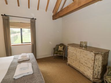 A bedroom with a bed folded towels on it a window with curtains a dresser and an armchair at Fairoaks Barns in Hollybush near Ledbury
