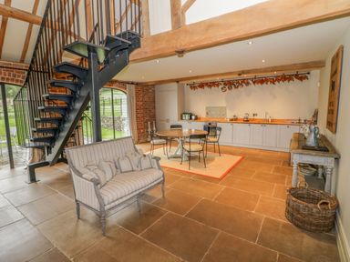A kitchen and dining area with a round table and chairs a metal staircase and a small sofa at Fairoaks Barns in Hollybush near Ledbury