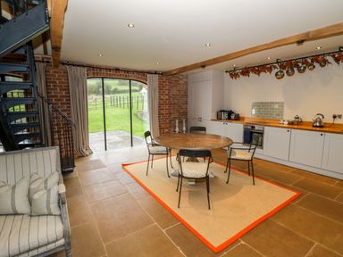A kitchen dining area with a round wooden table and four chairs on a rug near large windows at Fairoaks Barns in Hollybush near Ledbury