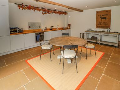A kitchen with a round wooden table and four chairs on a rug and cabinets along the wall at Fairoaks Barns in Hollybush near Ledbury