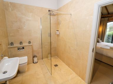 A bathroom with a shower area with a glass partition a toilet and a sink with a bedroom visible through the doorway at Fairoaks Barns in Hollybush near Ledbury