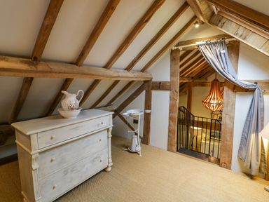 An attic room with wooden beams a white chest of drawers and a large light fixture at Fairoaks Barns Hollybush near Ledbury
