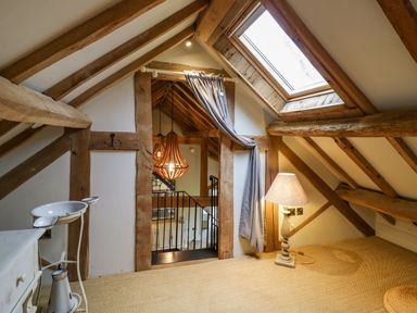 An attic room with exposed wooden beams a skylight a lamp and a small wash basin at Fairoaks Barns in Hollybush near Ledbury