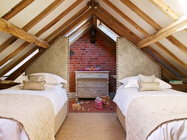 An attic bedroom with two single beds a wooden dresser and children's toys on the floor at Fairoaks Barns in Hollybush near Ledbury