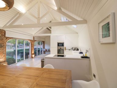 A kitchen and dining area with white cabinets wooden table large windows and exposed brick at Fairoaks Barns Hollybush near Ledbury
