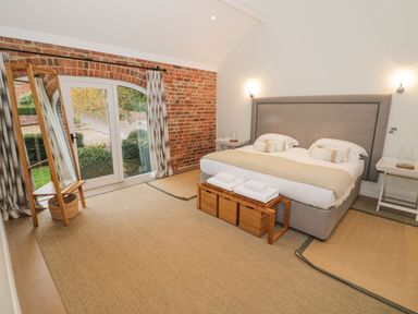 A bedroom with a double bed wooden bench and mirror near a glass door at Fairoaks Barns in Hollybush near Ledbury