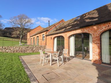 A patio with a table and four chairs outside a brick building with arched windows at Fairoaks Barns Hollybush near Ledbury