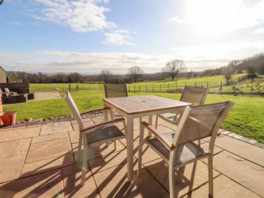 An outdoor patio with a table and four chairs overlooking a grassy field with trees at Fairoaks Barns in Hollybush near Ledbury