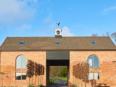 A brick building with arched windows and a clock tower with a weather vane at Fairoaks Barns in Hollybush near Ledbury