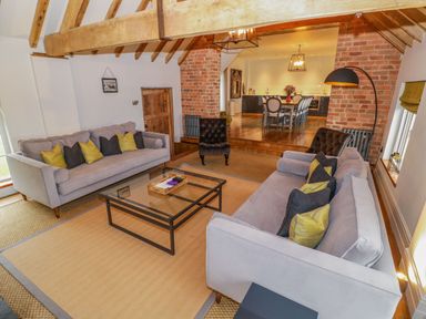 A living room with two sofas a glass coffee table and exposed beams next to a dining area at Fairoaks Barns in Hollybush near Ledbury