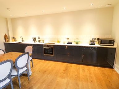 A kitchen with a wooden dining table and chairs and black cabinets with appliances at Fairoaks Barns in Hollybush near Ledbury