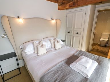 A bedroom with a bed white pillows and folded towels beside a bathroom at Fairoaks Barns in Hollybush near Ledbury