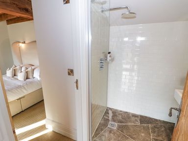 A bedroom with a bed and pillows next to a bathroom with a shower at Fairoaks Barns in Hollybush near Ledbury
