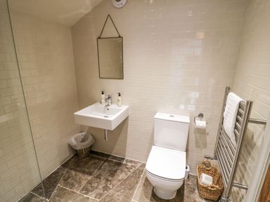 A bathroom with a wall-mounted sink mirror toilet towel radiator and a wicker basket on a tiled floor at Fairoaks Barns in Hollybush near Ledbury
