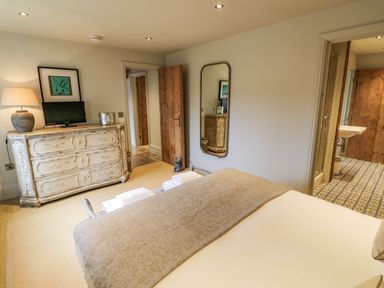 A bedroom with a bed covered in blankets a dresser with a lamp and television a wall mirror and an open door to a bathroom at Fairoaks Barns Hollybush near Ledbury