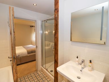 A bathroom with a sink and mirror next to a glass shower and an open door leading to a bedroom at Fairoaks Barns in Hollybush near Ledbury